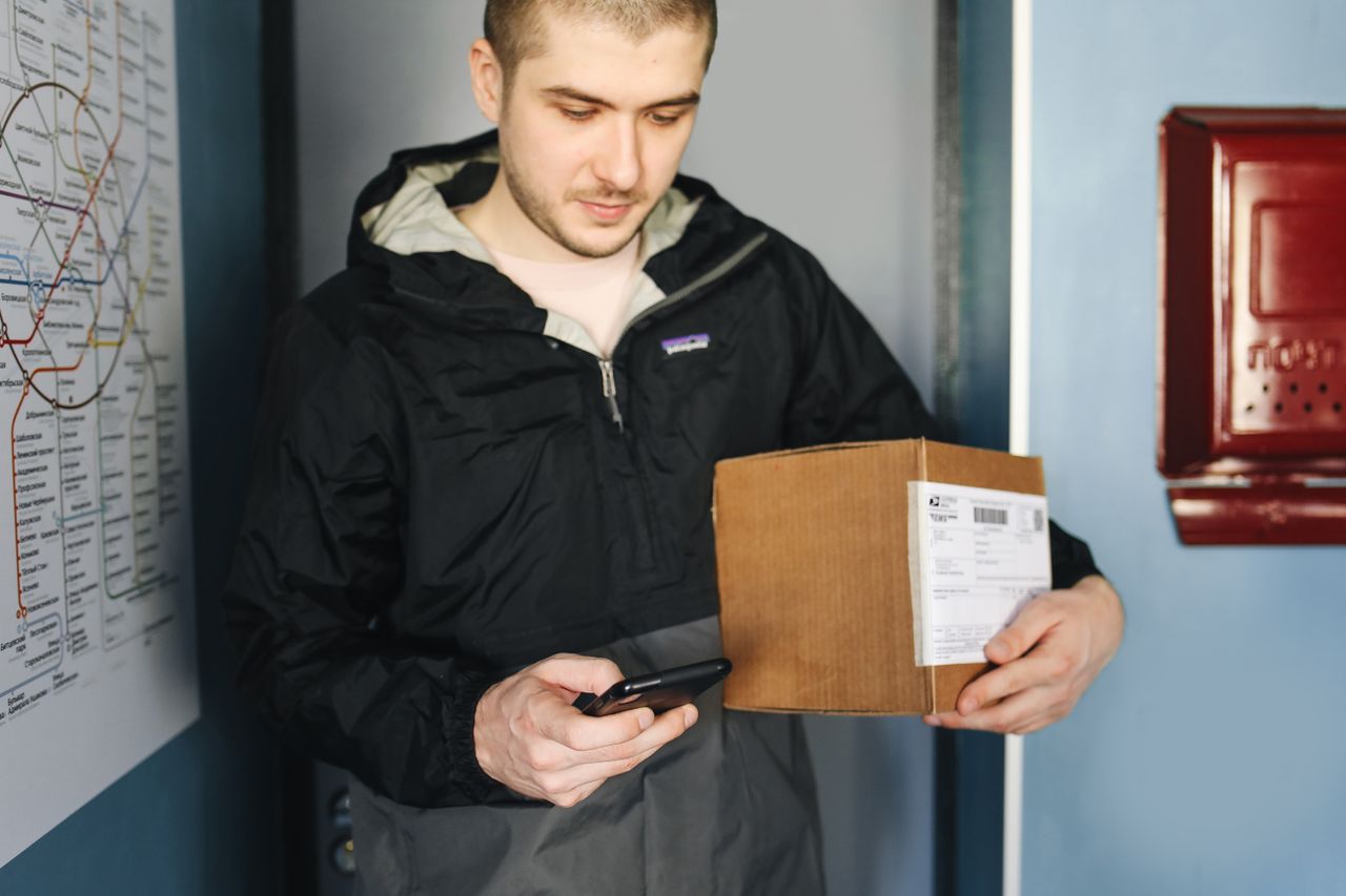 Services Man in casual jacket scans package label using smartphone indoors near metro map.