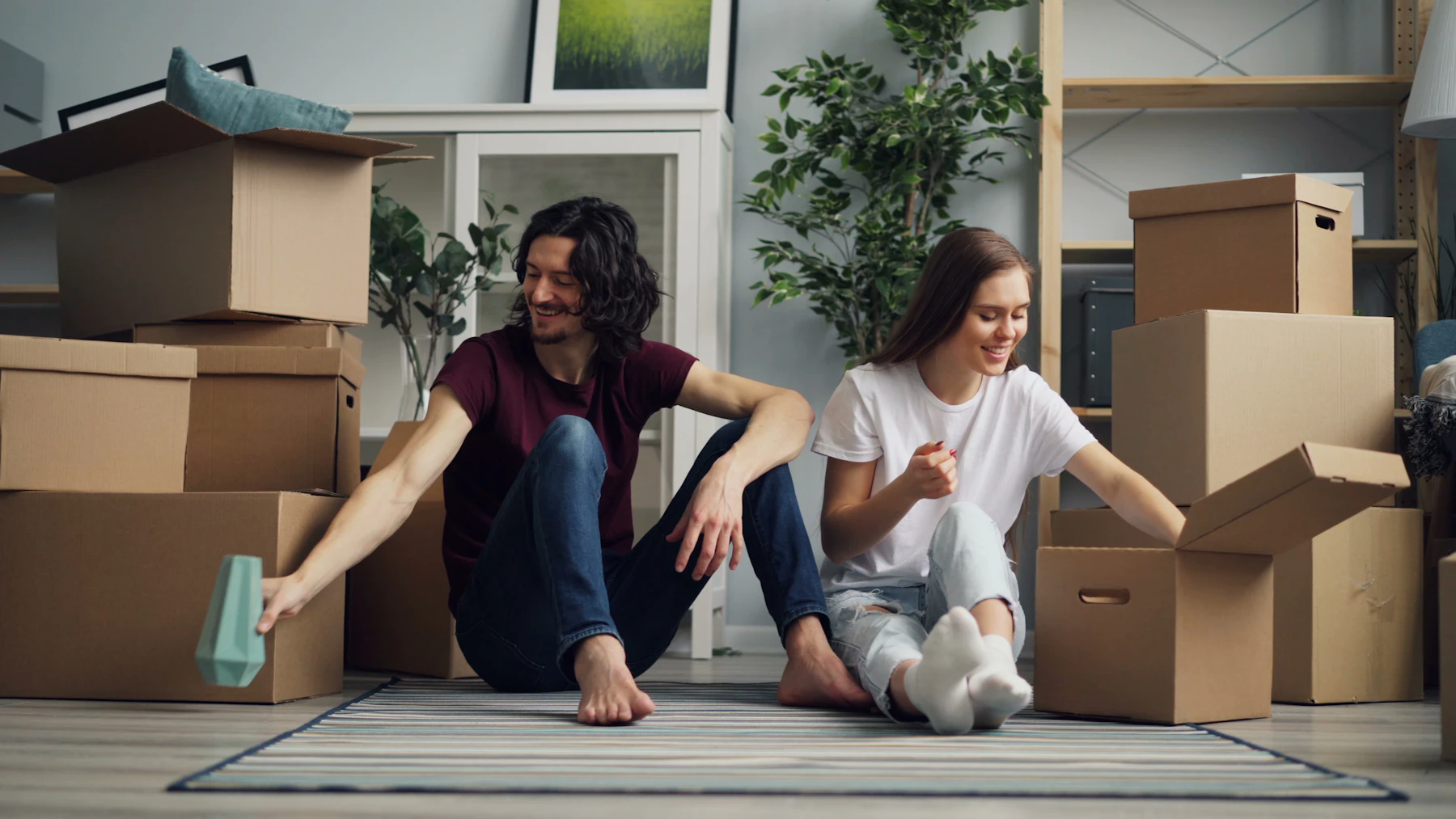 বাংলাদেশে কার্গো পাঠান — East End Logistics (বাংলা) Two people sitting on the floor surrounded by packed cardboard boxes